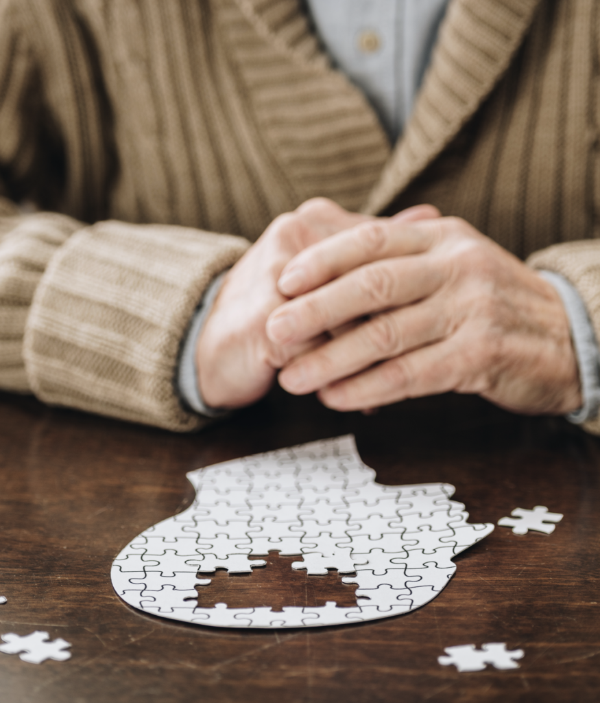 Dementia wellbeing club - mature hands over a jigsaw shaped like a human head, with pieces missing